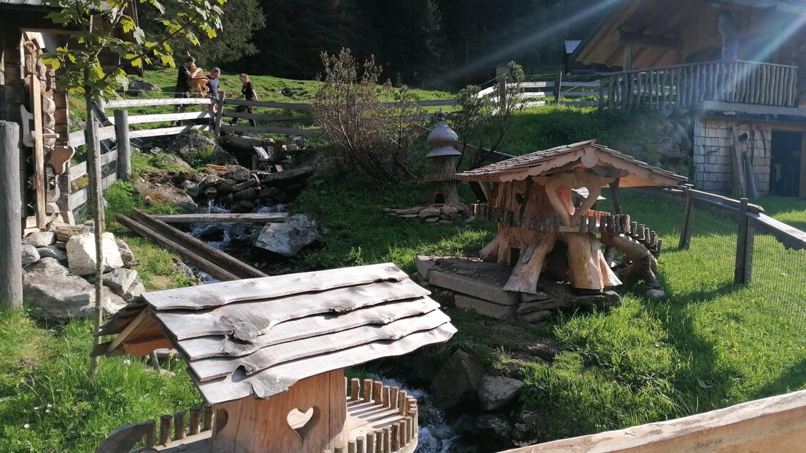 Eine idyllische Almhütte mit Holzelementen und einem kleinen Bachlauf. Umgeben von grünen Wiesen und Bäumen, strahlt die Szene eine ruhige Landatmosphäre aus. | © Nicole Leitgab