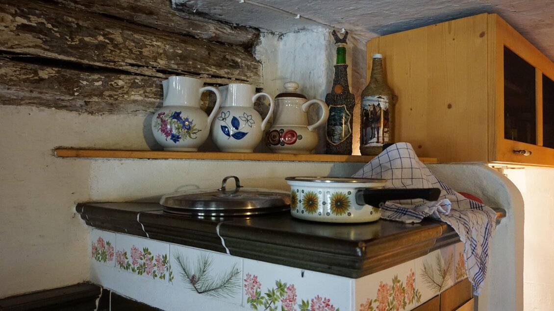 Eine rustikale Küche mit traditionellen Töpfen und Geschirr auf einem Holzregal. Die Wände sind mit hübschen Blumenmustern dekoriert. | © Nicole Leitgab