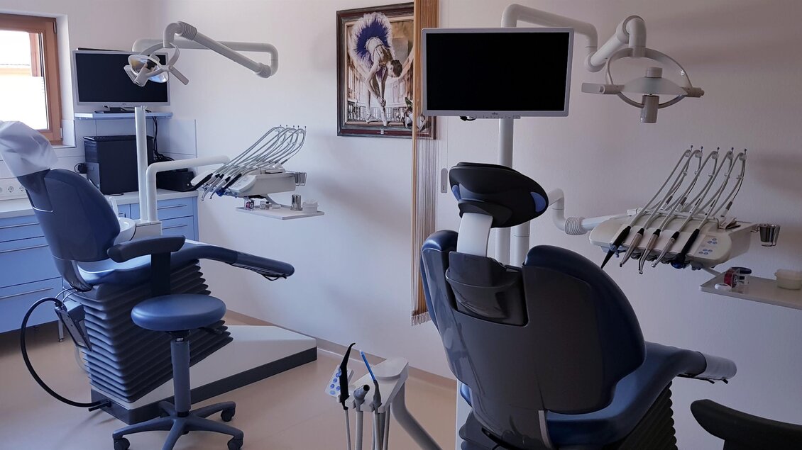 Eine zahnärztliche Praxis mit zwei Behandlungsstühlen und moderner Ausstattung. An der Wand hängt ein Bild, und der Raum ist hell und einladend. | © Dr. Szekely | Praxis