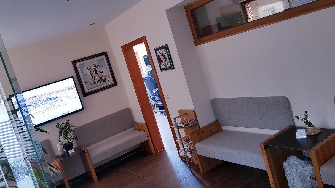 Ein moderner Empfangsbereich mit hellen Wänden und bequemen Sitzgelegenheiten. An der Wand hängt ein Fernseher und es gibt dekorative Pflanzen. | © Dr. Szekely | Praxis