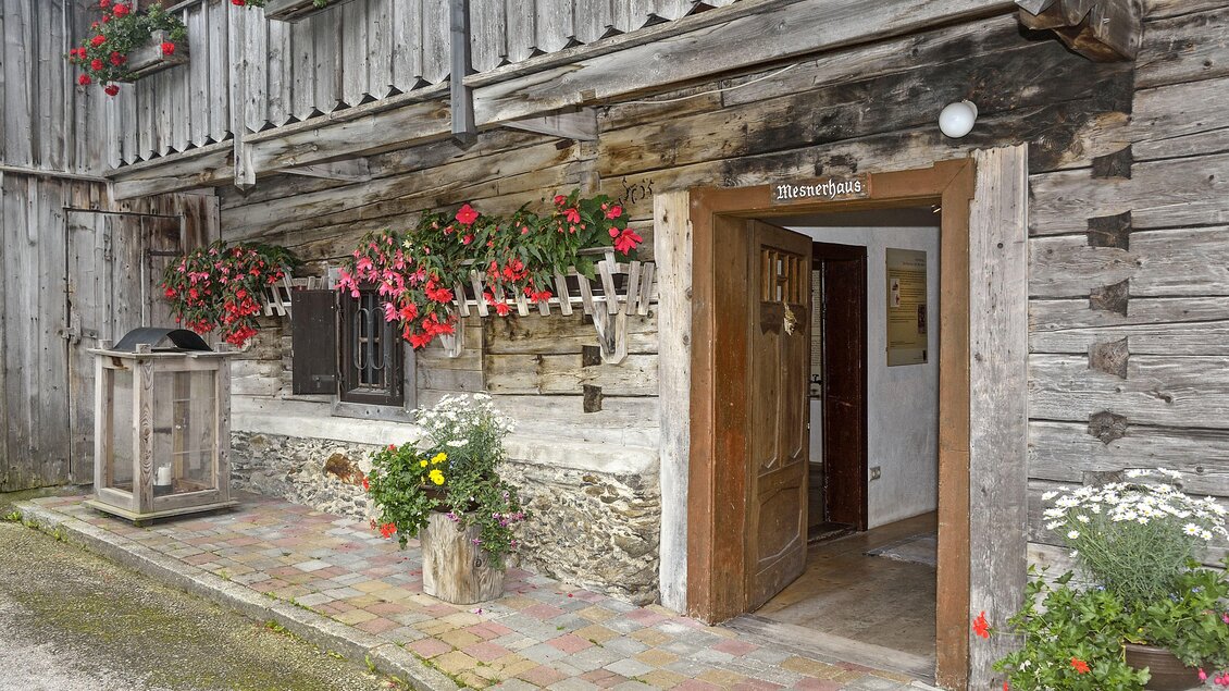 Ein gemütliches Bauernhaus mit Holzfassade und bunten Blumen. Die Eingangstür ist einladend und umgeben von einem gepflegten Pflaster. | © Herfried Marek