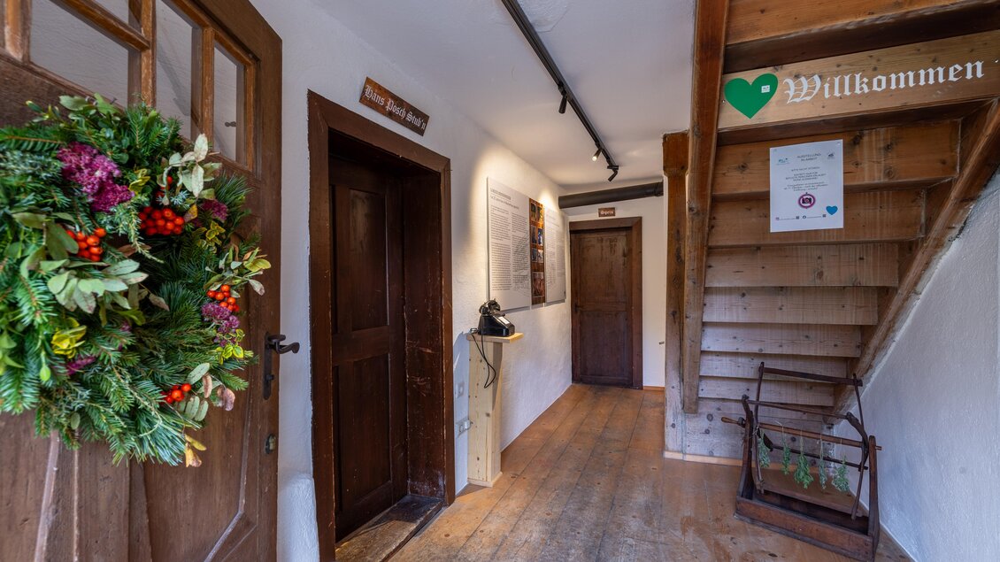 Ein einladender Flur mit Holzfußboden und einer weihnachtlichen Türkranz. Eine Treppe führt nach oben, und ein Schild mit "Willkommen" hängt an der Wand. | © Harald Steiner