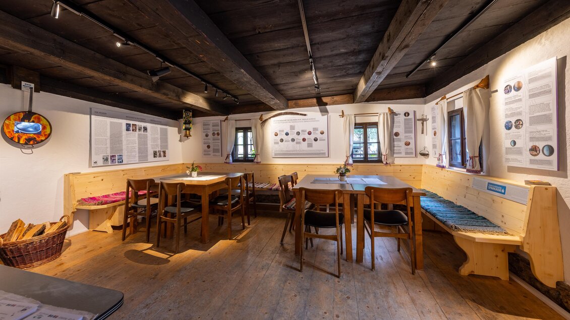 Ein rustikaler Raum mit holzverkleideten Wänden und Tischen. An den Wänden sind Informationsplakate angebracht, und große Fenster sorgen für Tageslicht. | © Harald Steiner