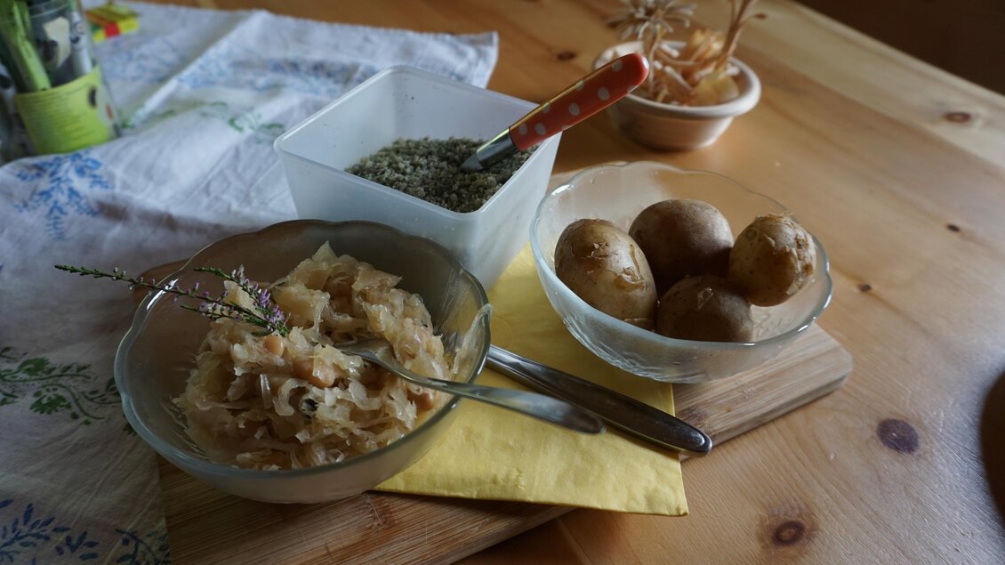 Ein rustikales Gericht mit Sauerkraut, gekochten Kartoffeln und Gewürzen auf einem Holzbrett. Die Tischdecke und Dekoration verleihen eine gemütliche Atmosphäre. | © Naturpark Sölktäler