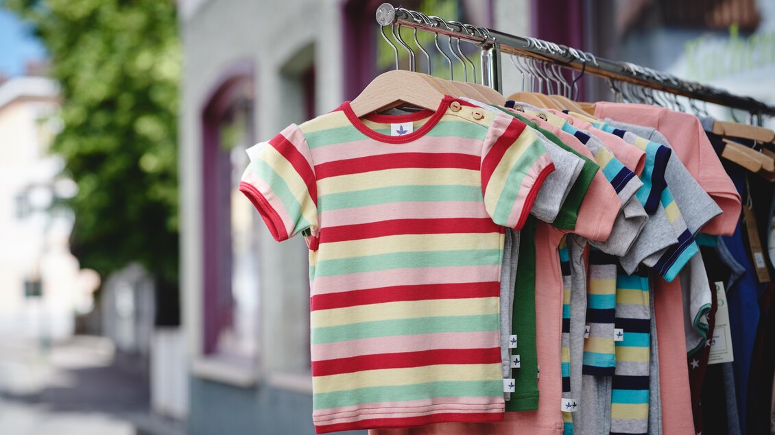 Ein bunter Bildschirm mit gestreiften T-Shirts hängt an einem Kleiderständer. Die Shirts in verschiedenen Farben sind ideal für Kinder. | © Liebstöckel