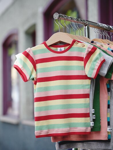 Ein bunter Bildschirm mit gestreiften T-Shirts hängt an einem Kleiderständer. Die Shirts in verschiedenen Farben sind ideal für Kinder. | © Liebstöckel