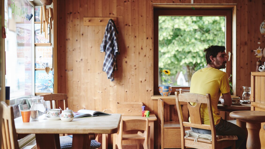 Ein gemütliches Café mit Holzverkleidung und einem großen Fenster. Ein Mann sitzt am Tisch und blickt nachdenklich hinaus. | © Liebstöckel