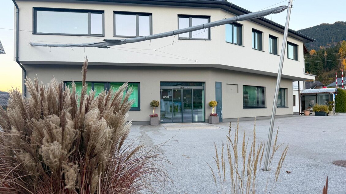 Ein modernes Gebäude mit großen Fenstern und einem begrünten Eingangsbereich. Im Vordergrund sind dekorative Pflanzen zu sehen. | © Gemeinde Sölk