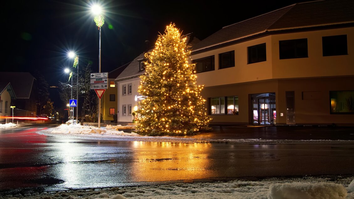 Ein festlich beleuchteter Weihnachtsbaum steht an einer Straße in der Nacht. Der Schnee auf dem Boden reflektiert das Licht und sorgt für eine winterliche Atmosphäre. | © Gemeinde Sölk