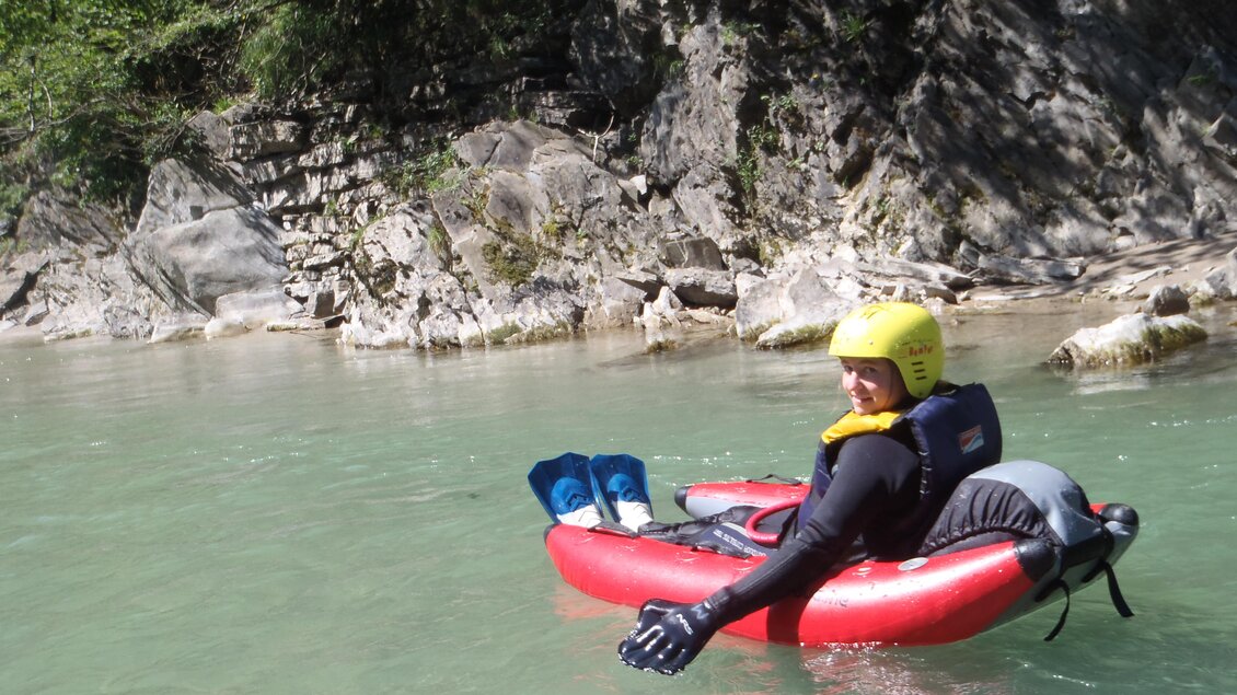 Ein Mensch sitzt in einem roten Schlauchboot im klaren Wasser. Im Hintergrund sind steinige Ufer und Bäume zu sehen. | © Thomas Humer