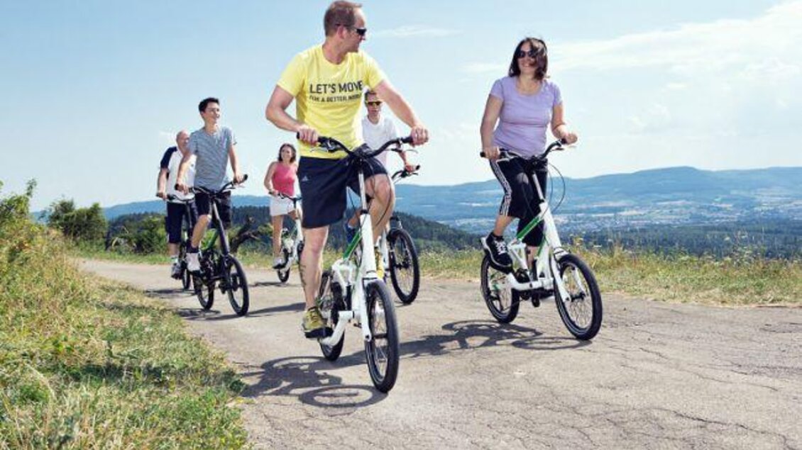 Eine Gruppe von Radfahrern fährt auf einem Feldweg. Die Sonne scheint und die Umgebung ist grün und hügelig. | © Thomas Humer