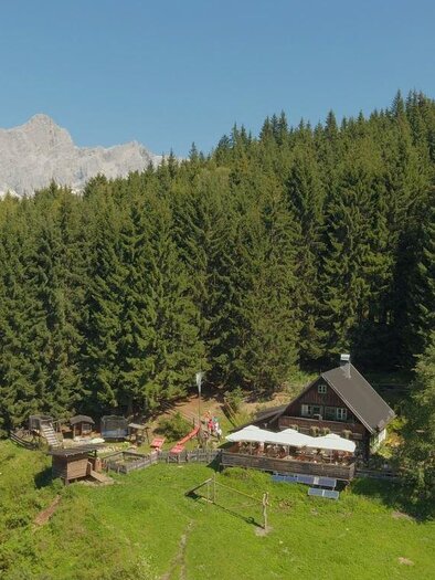 A picturesque mountain village surrounded by dense forests and majestic peaks. In the foreground, there is a cozy house with a terrace. | © Ochsenalm