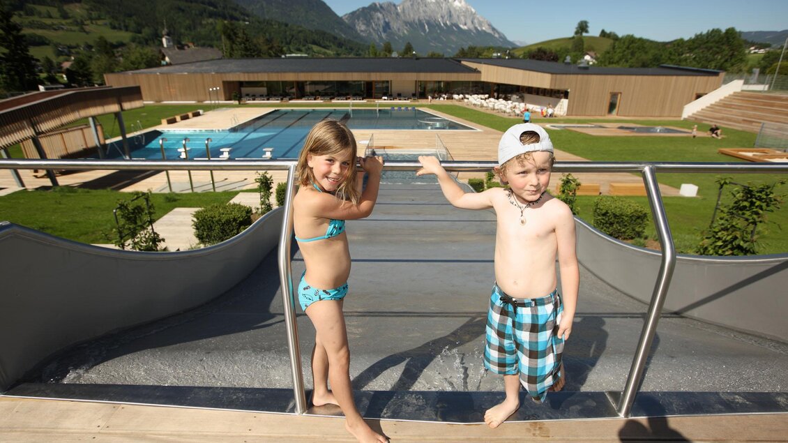 Zwei Kinder stehen am Rand eines Pools. Im Hintergrund sind Berge und viel Grün zu sehen. | © Panoramabad Gröbming