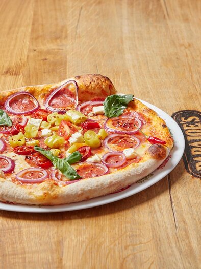 A freshly baked pizza with tomatoes, onions, and basil on a wooden board. The image shows an appetizing presentation of the pizza. | © PhotoINstyle - Brigit Steinberger