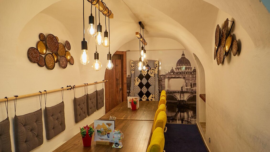 Ein stilvoller Raum mit einem langen Holztisch und bunten Stühlen. Die Wände sind dekoriert und es hängen moderne Lampen von der Decke. | © PhotoINstyle - Brigit Steinberger