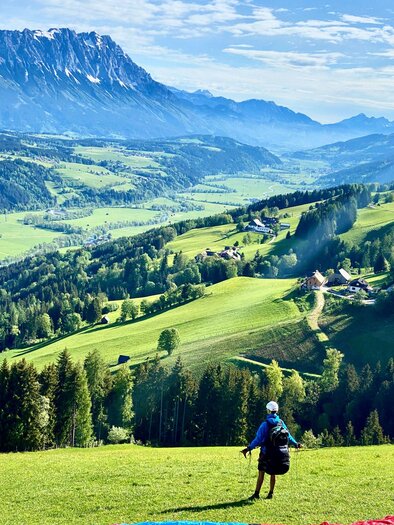 A picturesque landscape with lush green meadows and majestic mountains in the background. A person stands in the middle and enjoys the view. | © Sky Club Austria 