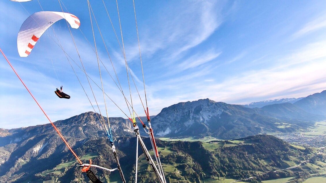Ein Paraglider schwebt über einer grünen Berglandschaft. Der Himmel ist klar mit sanften Wolken. | © Sky Club Austria 
