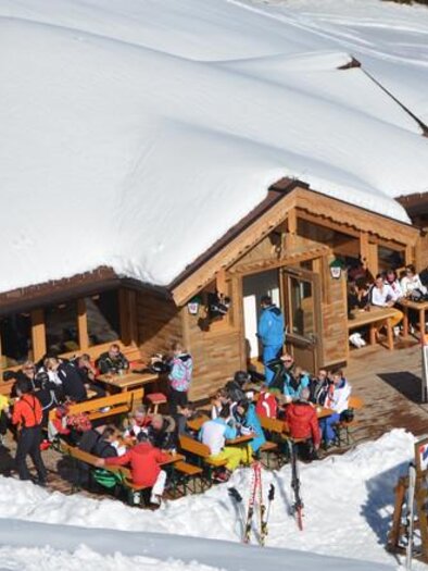 A cozy cabin in the snow, surrounded by a winter landscape. Many guests enjoy their time outside on the terrace. | © Pegasus