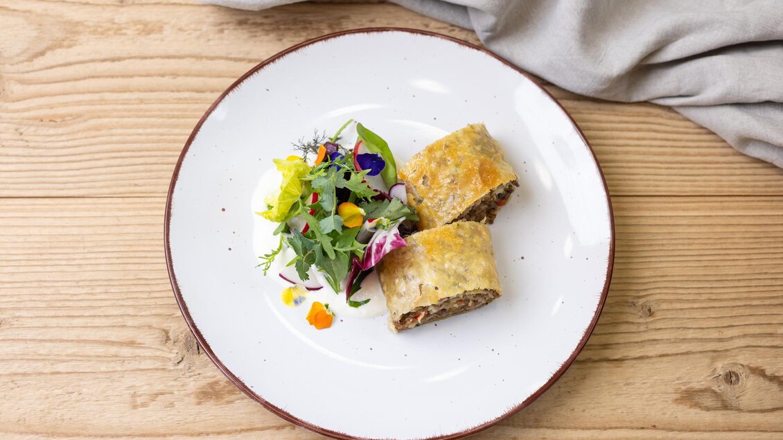 Ein Teller mit zwei Stücken gefülltem Blätterteig und einem bunten Salat. Dazu dekorative essbare Blumen und frische Kräuter. | © ©Martin Huber