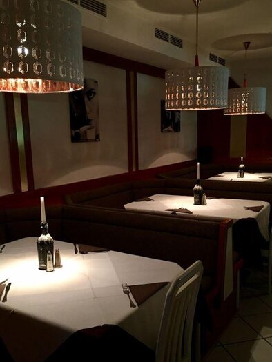 Elegant restaurant with dim lighting and modern lamps. The tables are neatly set with white tablecloths and candles. | © Amalfi