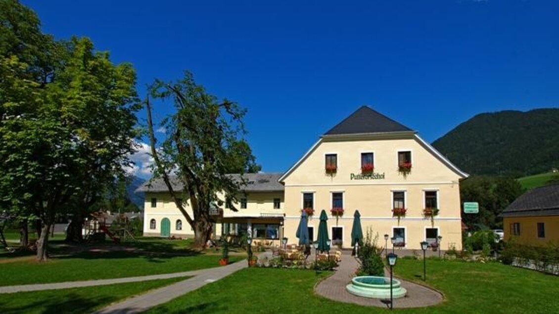 Ein schönes Hotelgebäude mit bunten Blumen und einem gepflegten Garten. Im Hintergrund sind grüne Berge und ein klarer Himmel zu sehen. | © Puttererseehof