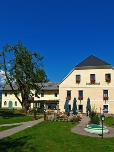 A beautiful hotel building with colorful flowers and a well-kept garden. In the background, green mountains and a clear sky can be seen. | © Puttererseehof