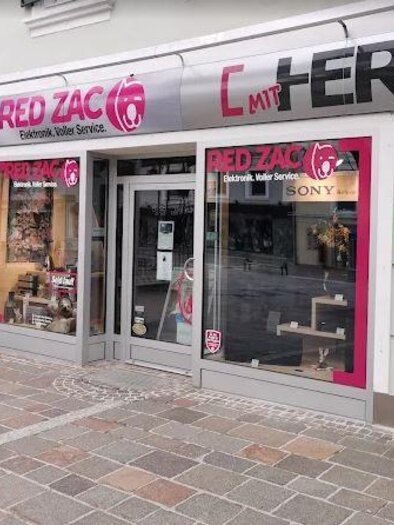 Ein Geschäft mit dem Namen "RED ZAC" bietet Elektronik und Service an. Die Fassade ist in Pink und Grau gestaltet, mit großen Schaufenstern. | © Michael Fischer