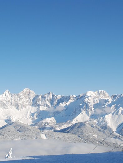 Eine schneebedeckte Berglandschaft mit strahlend blauem Himmel. Im Vordergrund ist ein Skilift zu sehen. | © Reiteralm Bergbahnen