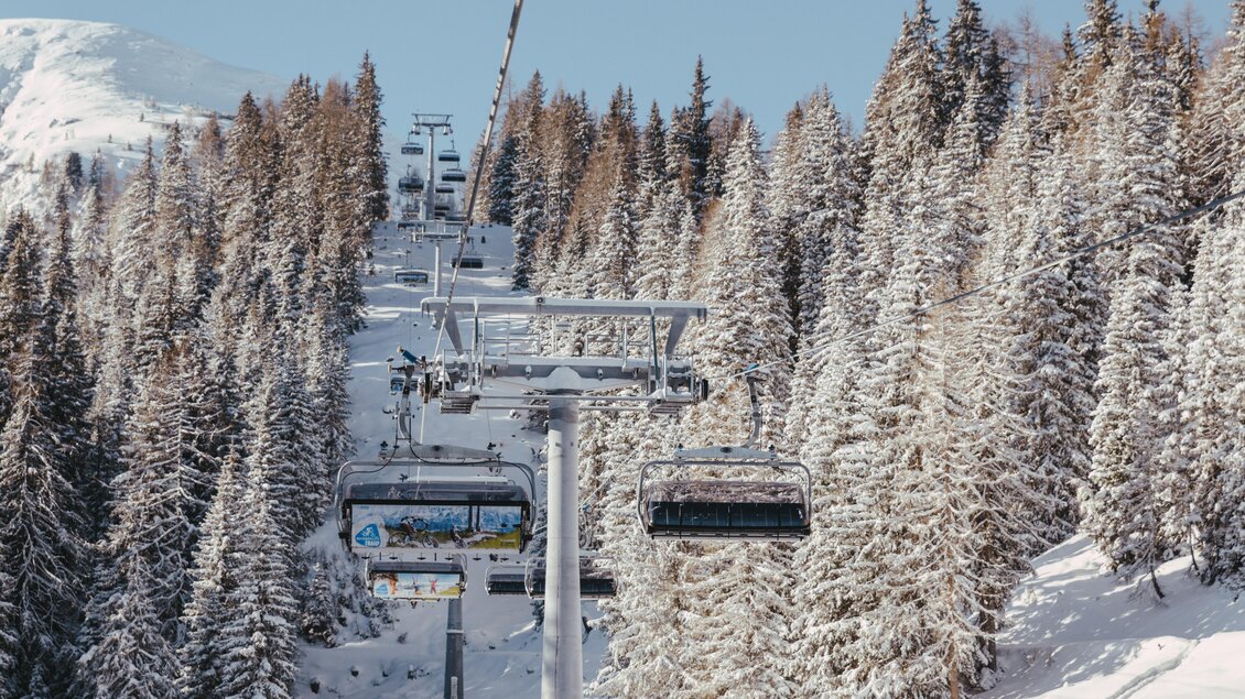 Eine Skiliftanlage führt durch verschneite Tannenbäume. Der Himmel ist klar und die Berglandschaft im Hintergrund ist majestätisch. | © Reiteralm Bergbahnen