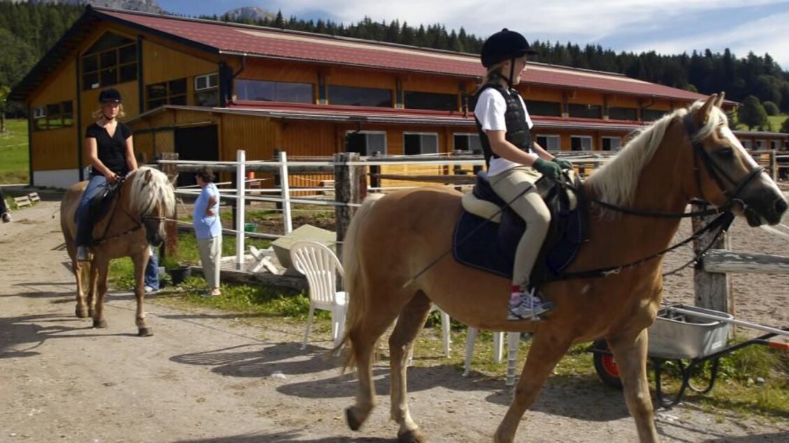 Reiterinnen auf Pferden genießen einen schönen Tag auf einem Reiterhof. Im Hintergrund ist ein modernes Stallgebäude und die Natur zu sehen. | © Zechmannhof