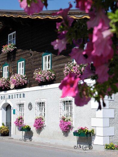 A charming building with a wooden facade and colorful flower boxes. The facade is decorated with many flowers, creating an inviting atmosphere. | © Reiters Wohlfühlhotel