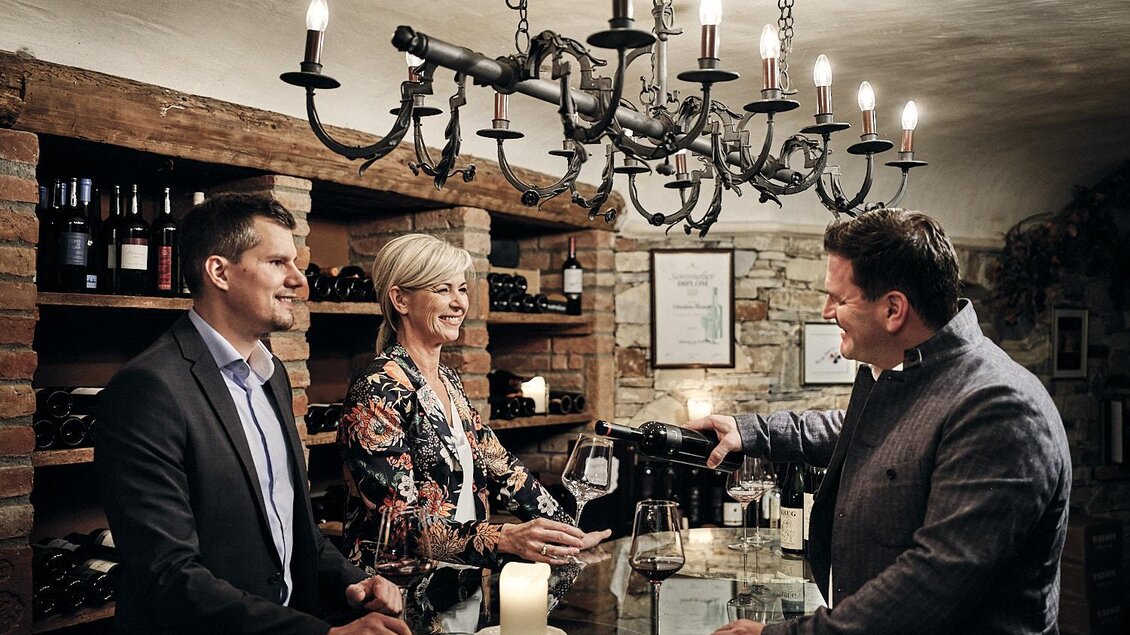 Ein geschmackvoll eingerichtetes Weinlokal mit einem eleganten Tisch. Drei Personen unterhalten sich, während einer von ihnen Wein serviert. | © Hotel Pichlmayrgut