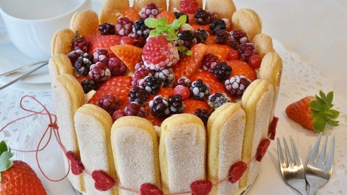 Eine farbenfrohe Torte mit Löffelbiskuits, frischen Erdbeeren und verschiedenen Beeren. Die Torte ist liebevoll dekoriert und sieht sehr einladend aus. | © Restaurant-Cafe Landgraf