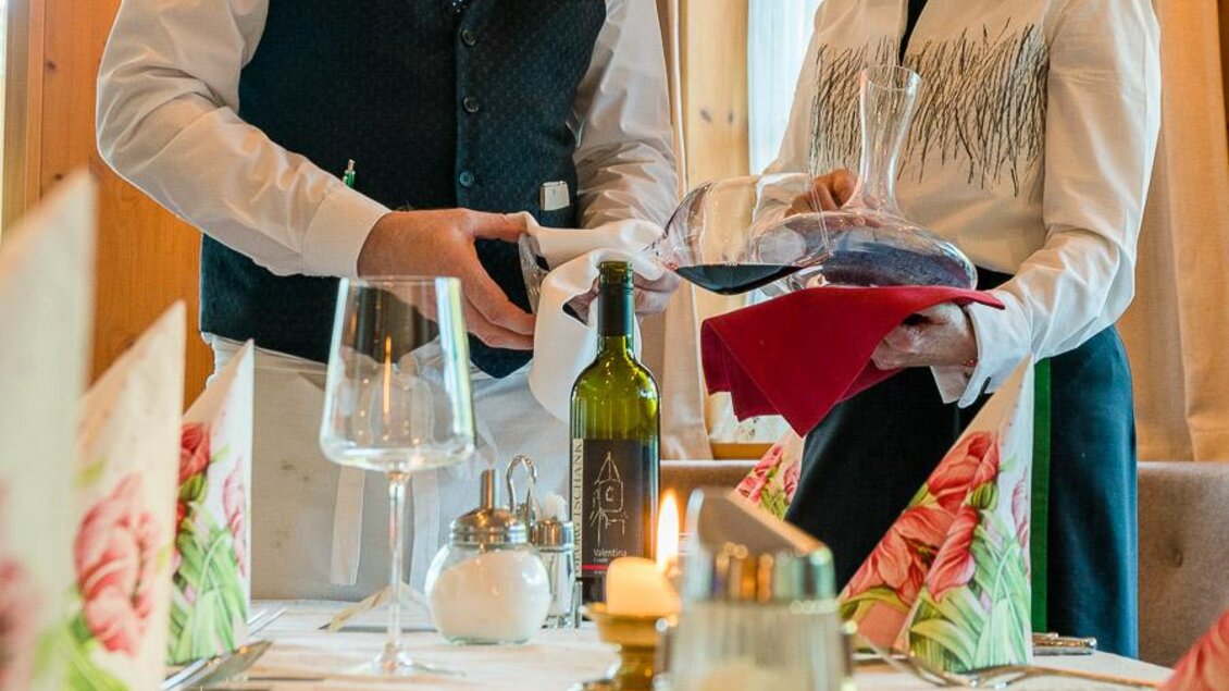 Ein elegantes Restaurant, in dem ein Kellner Wein dekantiert. Der Tisch ist liebevoll gedeckt mit Blumen und Kerzen. | © Restaurant-Cafe Landgraf