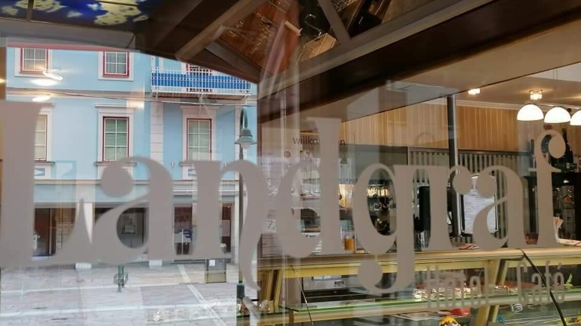 Ein Schaufenster mit der Aufschrift "Landgraf" zeigt verschiedene Backwaren. Im Hintergrund sind farbige Gebäude zu sehen. | © Restaurant-Cafe Landgraf