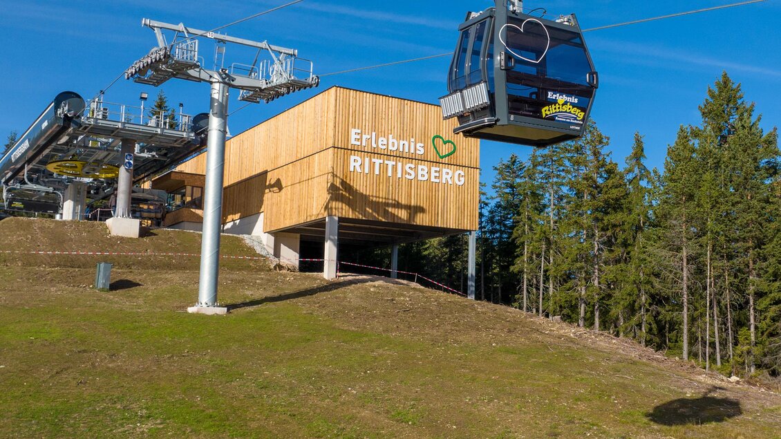 Eine Seilbahn schwebt über eine grüne Wiese in Richtung der Bergstation. Im Hintergrund sind Bäume und ein klarer blauer Himmel zu sehen. | © Hans-Peter Steiner