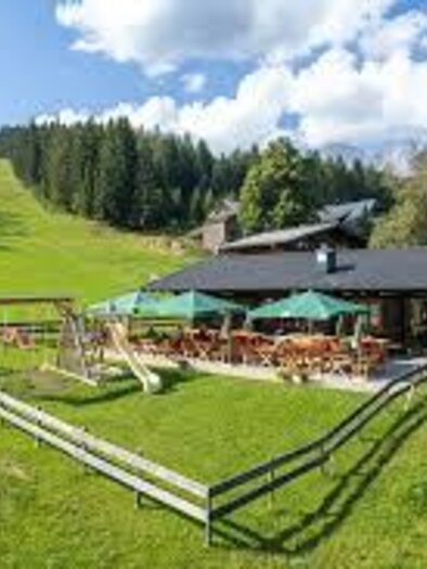 A beautiful playground on a hill with large letters that spell "RITTISBERG." In the background, an impressive mountain landscape stretches under a blue sky. | © Tischlberger