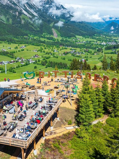 Eine schöne Berghütte mit vielen Sitzplätzen im Freien. Im Hintergrund sind grüne Wiesen und Berge sichtbar. | © Rittisstadl