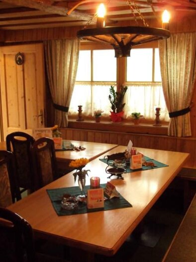 A cozy dining room with wooden decor and a large table. There are chairs, tablecloths, and plants for decoration. | © Roßstallbar