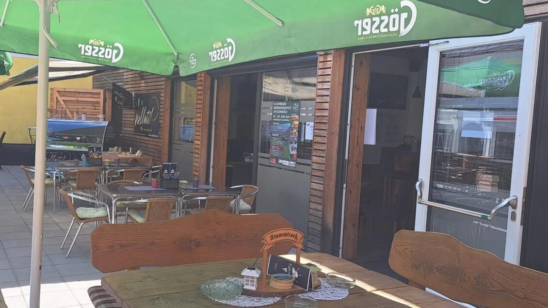 Ein gemütlicher Außenbereich eines Restaurants mit Holzdecken und grünen Sonnenschirmen. Die Tische sind liebevoll gedeckt und es gibt einen einladenden Eingang. | © Thomas Bartl