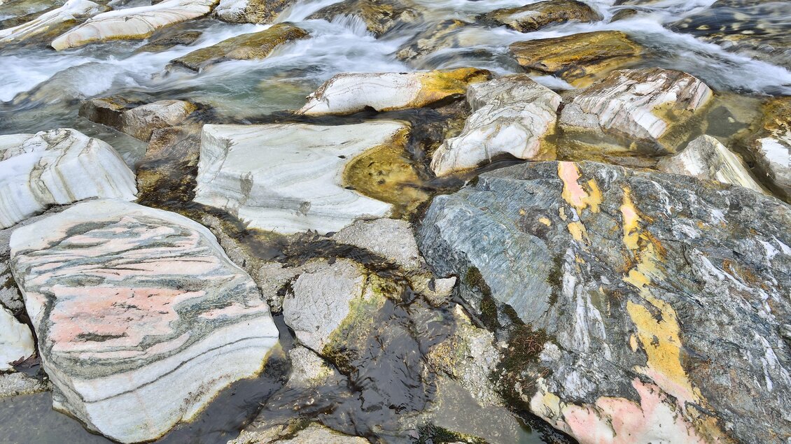 Ein Flussbett mit bunten, glatten Steinen und fließendem Wasser. Die Felsen zeigen verschiedene Farbtöne und Muster. | © Naturpark Sölktäler