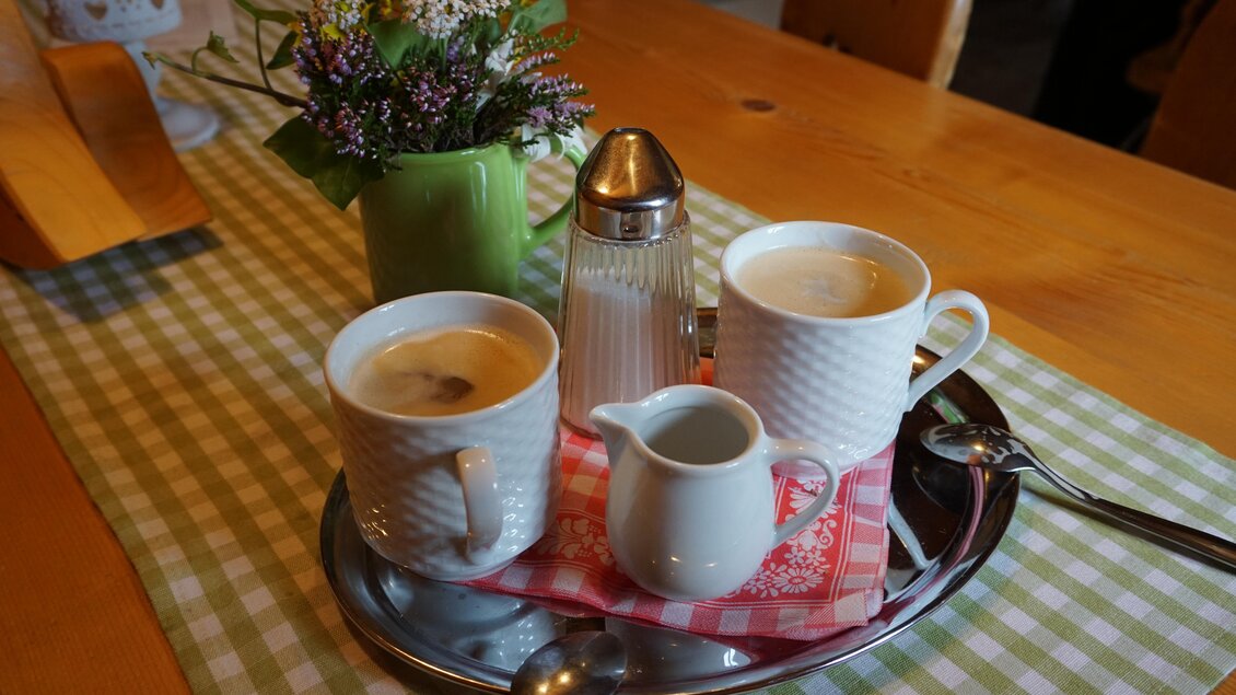Ein Tablett mit zwei Tassen Kaffee, einer Milchkanne und einer Zuckerdose steht auf einem karierten Tischdeckchen. Neben dem Tablett befindet sich eine kleine Blumenvase. | © Naturpark Sölktäler