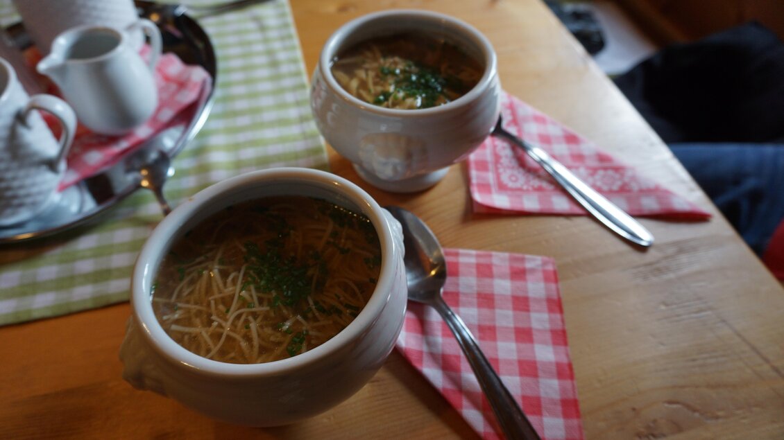 Zwei Schalen heißen Nudelsuppe stehen auf einem Holztisch. Sie sind mit frischem Schnittlauch garniert und umgeben von karierten Servietten. | © Naturpark Sölktäler