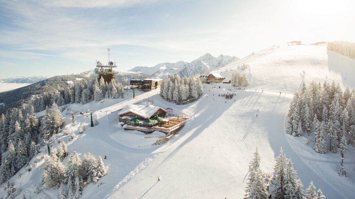 Eine schneebedeckte Landschaft mit einem Skigebiet und einem modernen Lift. Im Hintergrund sind Berge und Wälder zu sehen. | © Dominik Steiner