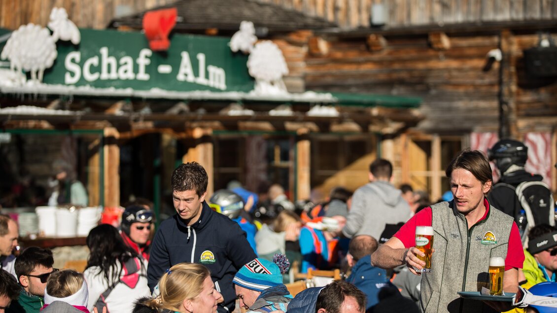 Eine belebte Skihütte mit vielen Gästen im Freien. Die Bedienung serviert Getränke und es herrscht eine fröhliche Atmosphäre. | © Harald Steiner