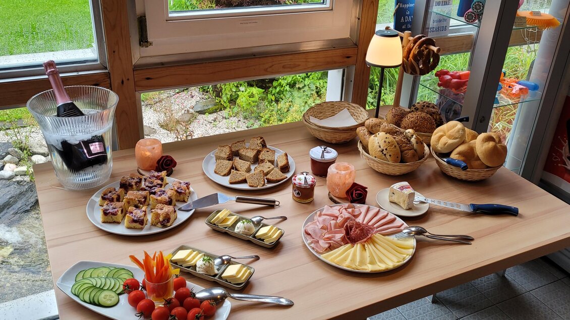 Ein liebevoll gedeckter Tisch mit verschiedenen Snacks und Köstlichkeiten. Es gibt Käse, Wurst, Gemüse, Brot und süße Leckereien in einem hellen, einladenden Raum. | © Tim Fuchsberger