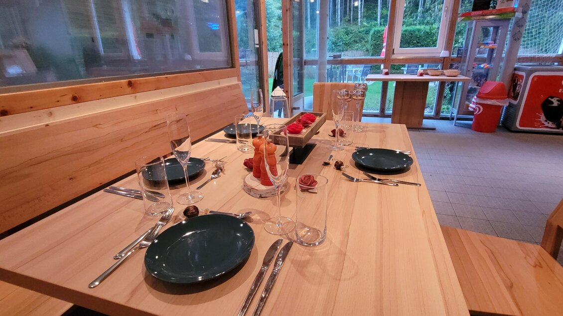 Ein schön gedeckter Tisch in einem modernen Holzraum. Auf dem Tisch befinden sich Teller, Gläser und Dekoration. | © Tim Fuchsberger