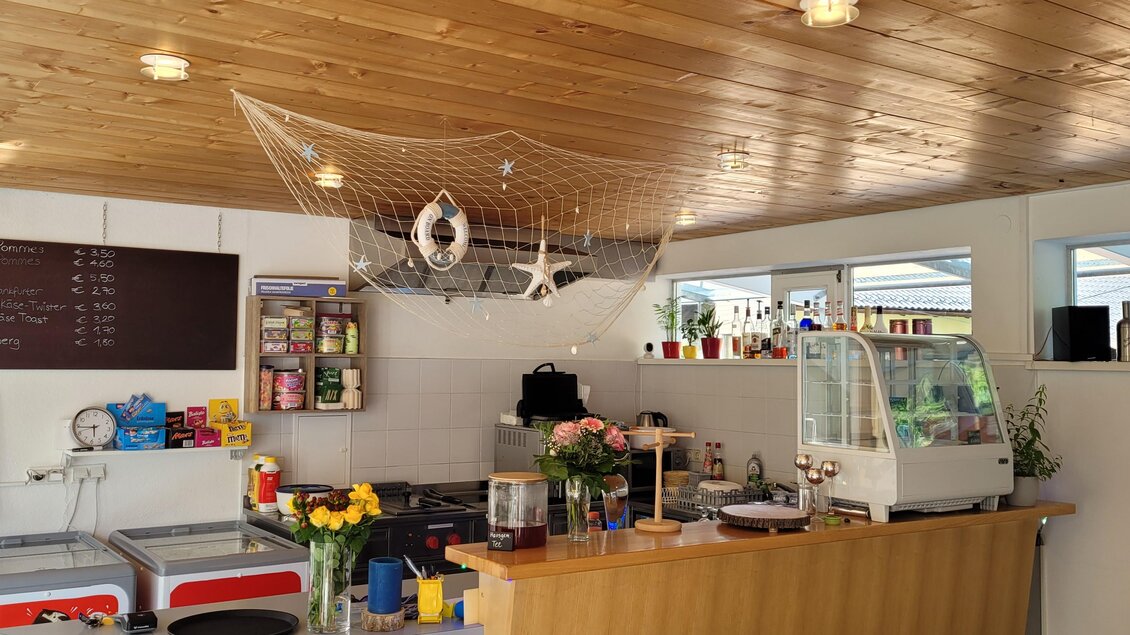 Ein gemütlicher Caféraum mit Holzdecken und einer einladenden Theke. Im Hintergrund sind verschiedene Getränke und Snacks sichtbar. | © Tim Fuchsberger