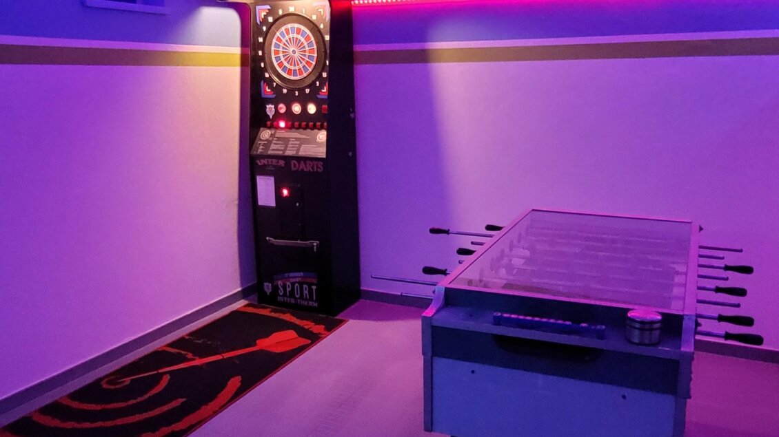 Ein moderner Spielbereich mit einem Dartautomat und einem Tischkicker. Die Beleuchtung in lila sorgt für eine entspannte Atmosphäre. | © Tim Fuchsberger