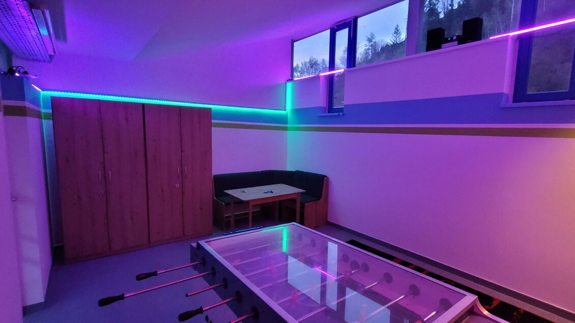 Ein moderner Raum mit neonfarbiger Beleuchtung. Im Vordergrund ist ein Tischfußballtisch zu sehen, und im Hintergrund befinden sich eine Sitzgelegenheit und Fenster. | © Tim Fuchsberger